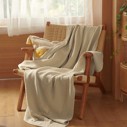 Beige GentleSoft 100% cotton gauze throw blanket draped on a woven chair with tasseled pillow.