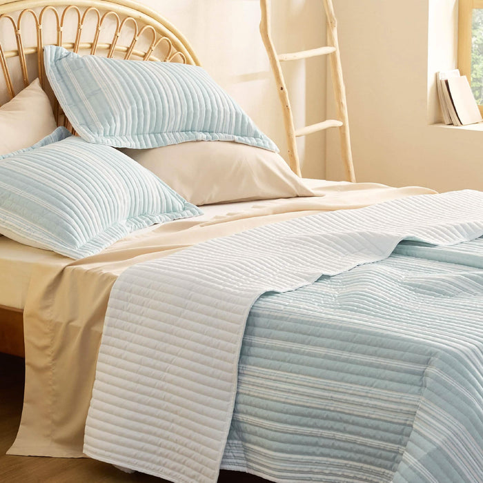 GentleSoft Chill Vibes Quilt Set light blue white stripes textured on bed wicker headboard.
