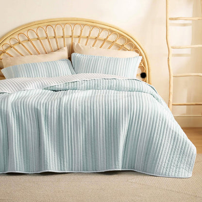 GentleSoft Chill Vibes Quilt Set, light blue & white ribbed microfiber, on bed w/ rattan headboard & beige pillows.