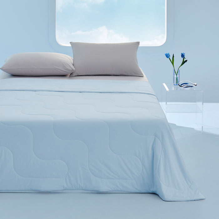 Light blue GentleSoft cooling blanket with wavy stitching on a bed with two grey pillows. Bedroom setting.