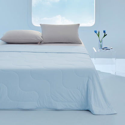 Light blue GentleSoft cooling blanket with wavy stitching on a bed with two grey pillows. Bedroom setting.