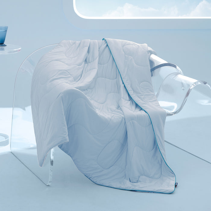 Light blue GentleSoft cooling blanket with wavy stitching and turquoise piping draped on a clear chair.