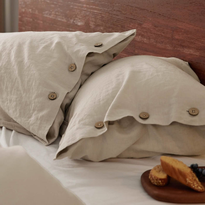 GentleSoft light beige cotton linen pillow covers with natural wood buttons on a cozy bed.