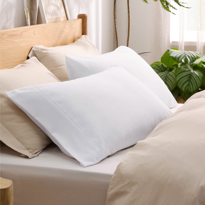 Two white GentleSoft microfiber pillowcases with envelope closure on a bed with neutral bedding and plants.