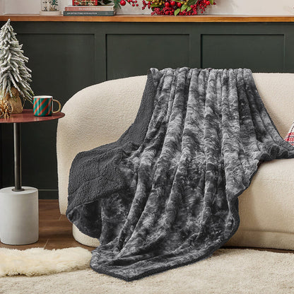 Dark grey reversible GentleSoft Faux Fur Sherpa fleece blanket draped over a cream sofa, showcasing plush texture.