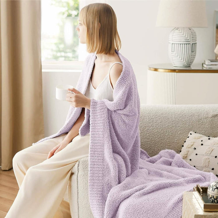 GentleSoft light lavender feather yarn throw blanket, cozy textured knit, draped over a woman holding a mug on a couch.