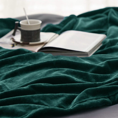 Deep forest green GentleSoft flannel fleece blanket draped on a bed with an open book and mug, showcasing plush texture.