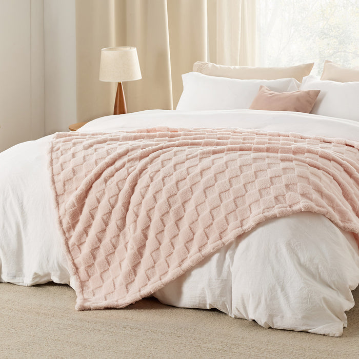 GentleSoft Jacquard Sherpa Blanket in light pink draped on a bed, showing plush texture and checker pattern.