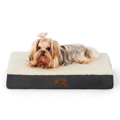 Small fluffy dog with pink bow relaxing on a large gray and cream orthopedic dog bed.