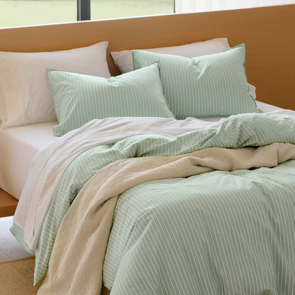 Sage green washed cotton duvet cover and pillow shams with white stripes, plus a beige quilted throw.