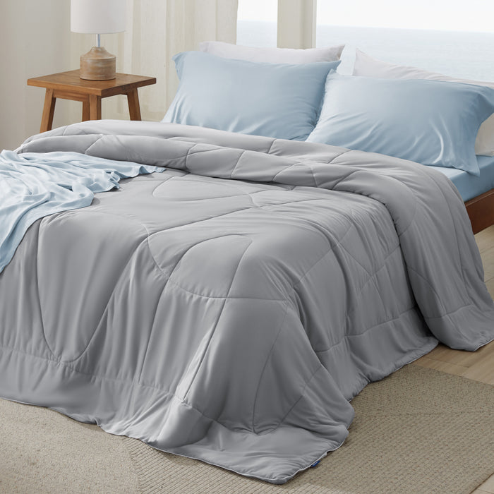 Grey Nylon Cooling Comforter draped on a bed with light blue accents. Lightweight and soft.