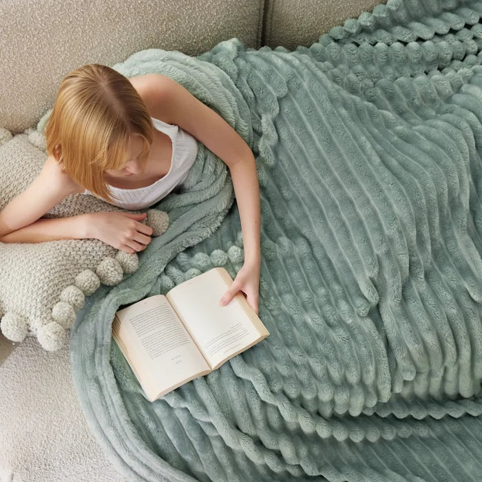 Soft ribbed sage green blanket draped over woman reading. Rayon Derived From Bamboo Modern Cozy Bundle.