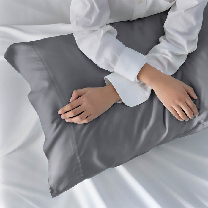 Hands touching charcoal grey GentleSoft rayon bamboo pillowcase, showcasing smooth, cool texture for skin and hair.