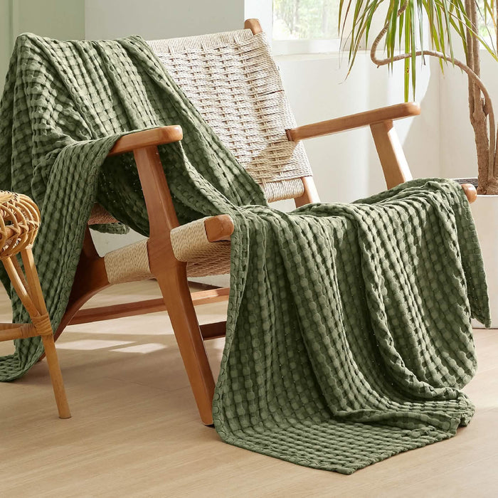Olive green GentleSoft waffle blanket on wooden chair. Bamboo-cotton blend, textured weave. Lifestyle shot.