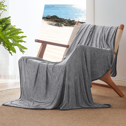 Gray GentleSoft reversible cooling blanket, nylon material, draped on a chair with a serene beach view.