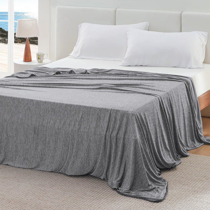 Gray GentleSoft reversible cooling blanket with subtle texture draped on a bed with ocean view. Nylon material.