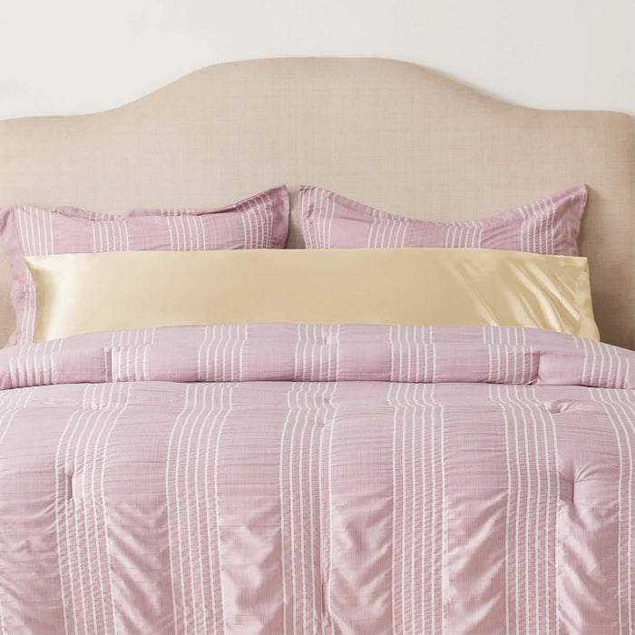 GentleSoft Satin Body Pillowcase in soft gold, placed horizontally on a bed with pink and white striped bedding.