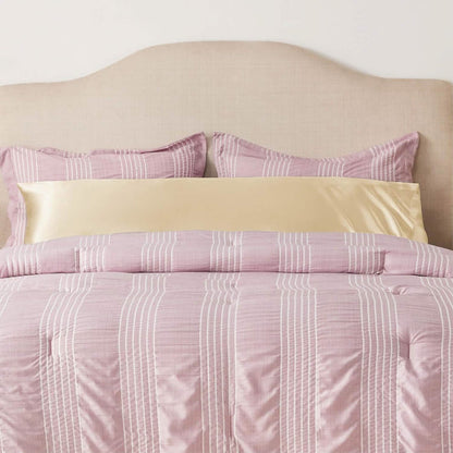 GentleSoft Satin Body Pillowcase in soft gold, placed horizontally on a bed with pink and white striped bedding.
