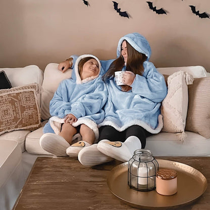 Women in light blue sherpa fleece wearable blankets relax on a couch, one holding a mug. Cozy comfort, hands-free design.