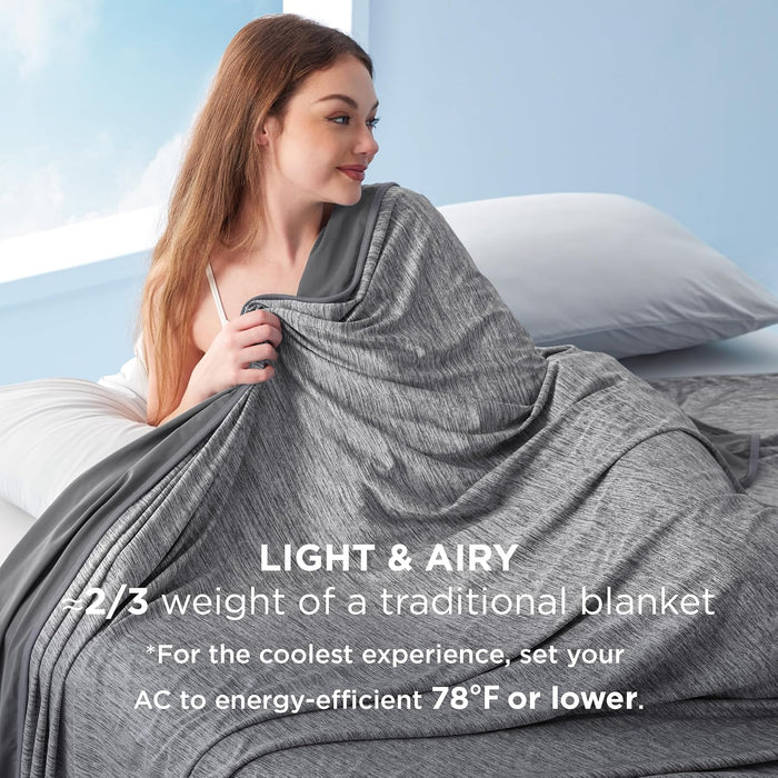 Woman wrapped in a lightweight, gray cooling blanket on a bed, noting 'Light & Airy, 2/3 weight'.